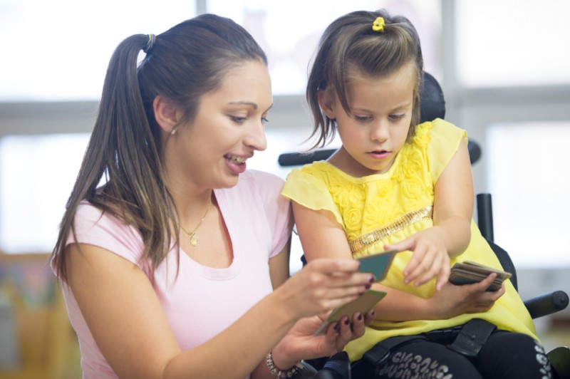 A tutor is helping a handicap girl learn at school with flash cards.